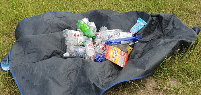 Svart presenning på gräs med utspridda tomma plastflaskor och förpackningar.