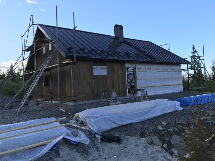 Byggarbetsplats med pågående fasadarbete på hus, ställningar, isoleringsmaterial och fasadnätarskåp.