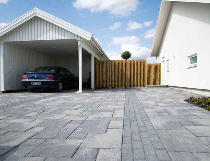 Uppfart med romanumönstrad betongsten bredvid modernt hus och carport.