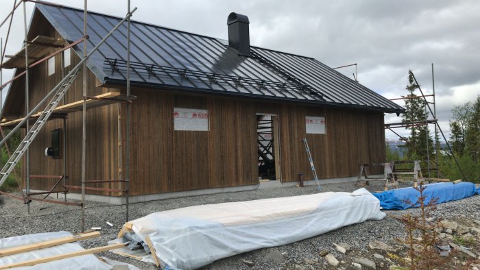 Nybyggt hus med träpanel och svart tak, byggmaterial ligger utanför.