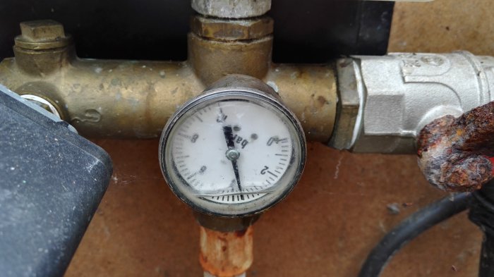Tryckmätare för vattenpump med avläsning på ca 1.5 bar, omgiven av rörledningar och korrosion.