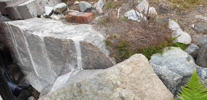 Stor sten som har delats med borrat hål längs mitten, omgiven av mindre stenar och vegetation.