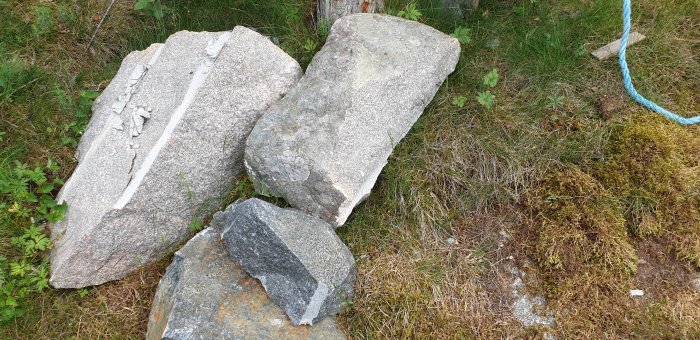 Stora borrande stenblock i gräs med synliga borrspår, omgivna av mossig mark.