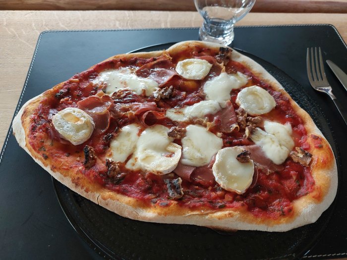 Hemlagad pizza med tomatsås, skinka, getost, valnötter och mozzarella på en svart tallrik.