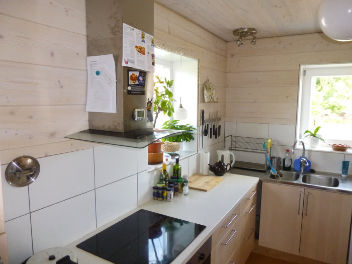 Kök med vit hårdvaxoljad träpanel på väggar, kakel ovanför arbetsbänkar och moderna köksapparater.