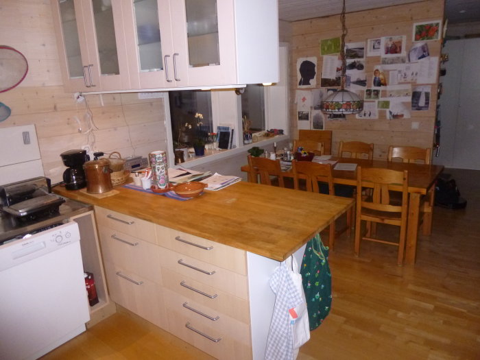 Kök med liggande träpanel på väggarna, träbänk, skåp och matbord med stolar.