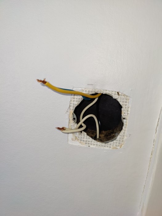 Öppen väggdosa med en gul och blå sladd uthängande, två vita sladdar, och en svart sladd, utan dimmer installerad.