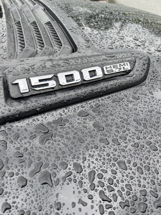 Närbild på en våt svart bildörr med "1500 HEMI 5.7" emblem och vattendroppar.