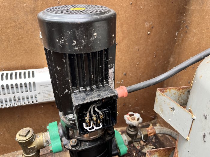 Elanslutningar i en öppen elektrisk dosa på en svart industriell pump med synliga rostiga delar och kablar.