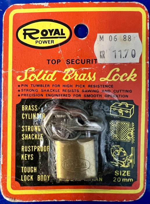 Nyckellås i mässing på förpackning, prislapp, beskrivning av pick resistance och rostskydd.