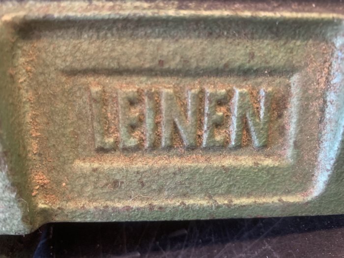 Närbild på en föremål med texten "LEINEN" i relief, täckt av rost och patina.