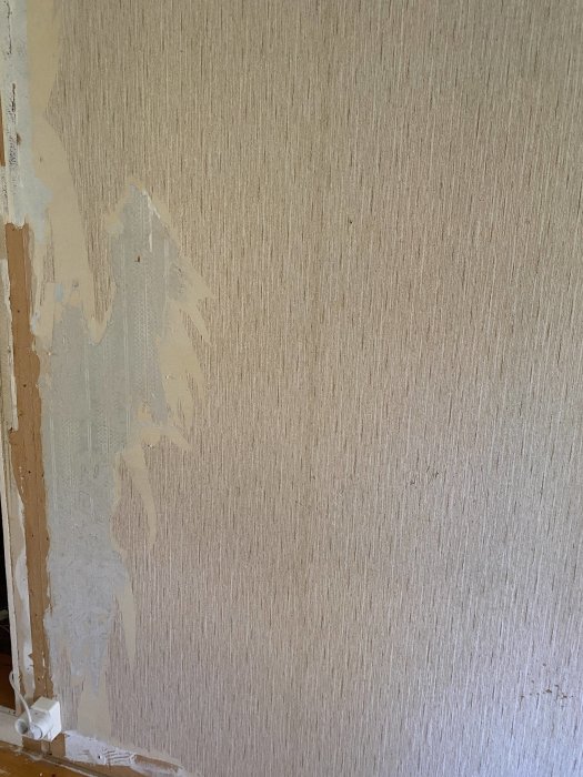 Vägg med avrivna tapetlager som exponerar ojämna sågspånsskivor under.