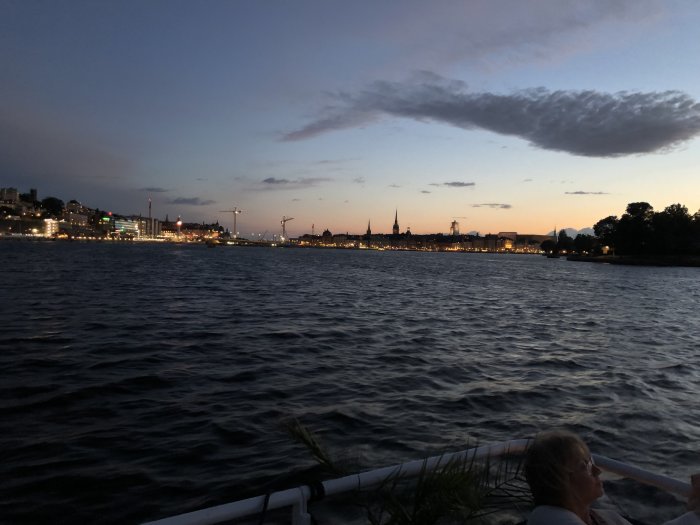 Stadssilhuett vid skymning sett från en båt på vattnet, med mörka vågor och himmel.
