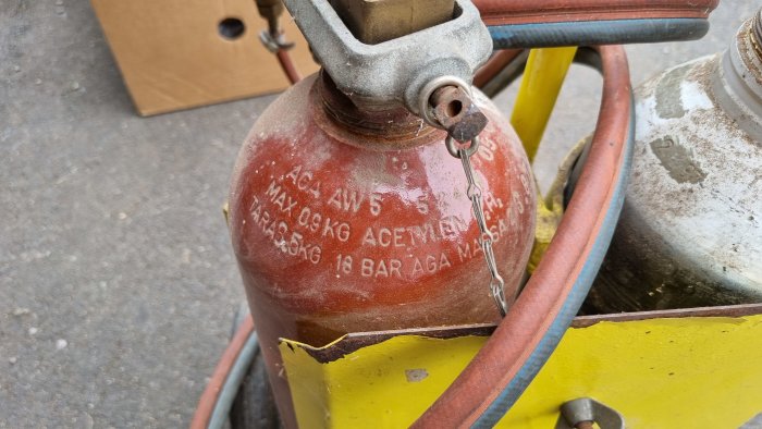 Närbild av en äldre röd acetylen gasflaska utan skyddskåpa, märkt med maxtryck och volym.