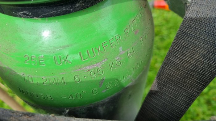 Närbild av en grönmålad gassvetsflaska etiketterad LUXFER med specifikationer ingraverade på ytan, visande tydlig avsaknad av skyddskåpa.