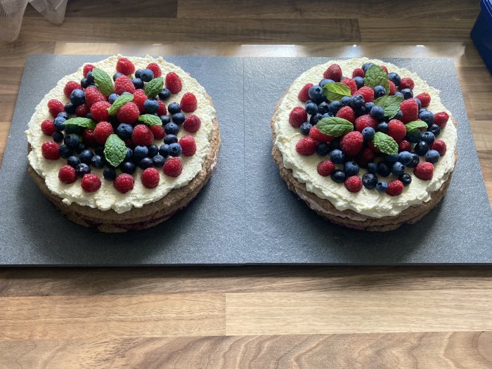 Två runda tårtor dekorerade med bär och myntablad på en grå skärbräda.