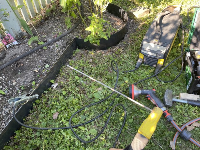 Rabattkanter av svart metall under montering i trädgård, med svetsverktyg och kapade metallbitar.