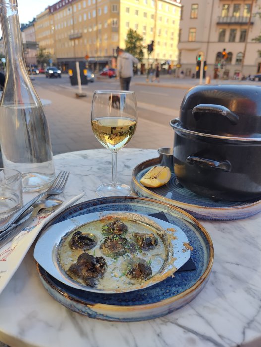 En tallrik med escargot och ett glas vitt vin på en restaurangterrass.