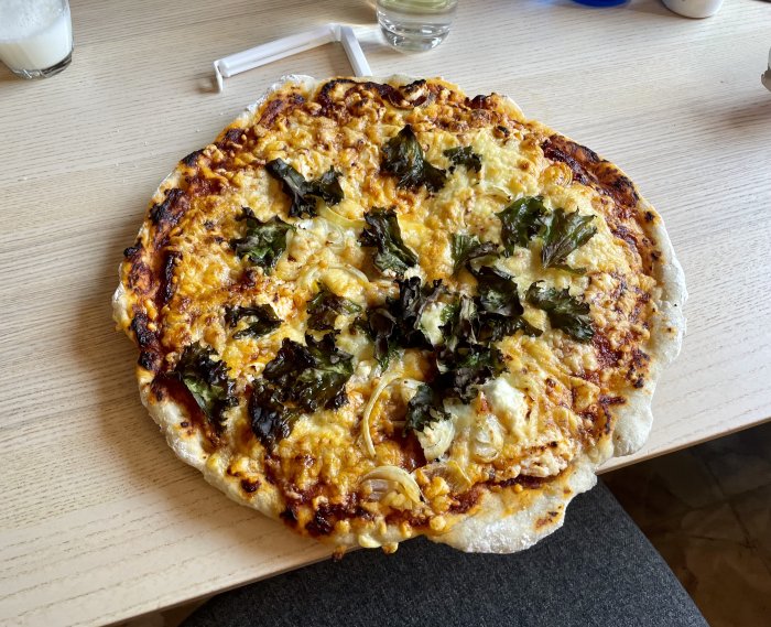 Hembakad pizza med gyllen ost och grönkål på trädgårdsbord.