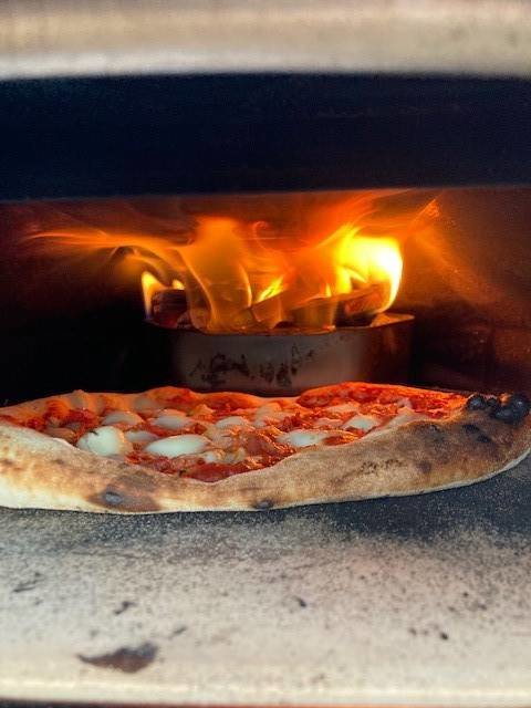 En pizza inne i en vedeldad ugn med synliga lågor och glöd från brinnande träbitar.