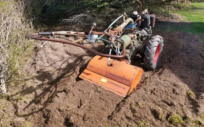 Jordfräs fastsatt vid baksidan av en traktor som fräser upp jord på ett fält.