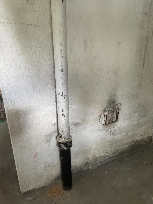 Vertikalt gjutjärnsavloppsrör som möter betonggolv och kopplas till PVC-rör med koppling.