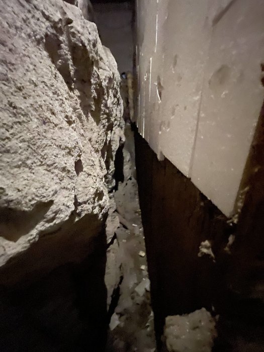 Mörk och trång krypgrund där kabeldragning för pump planeras, synliga stenfundament och isolering.
