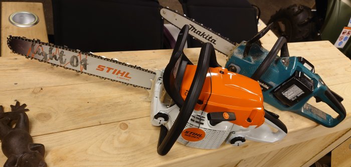 En Stihl 261 bensindriven motorsåg bredvid en Makita DUC353 batteridriven såg på ett bord.