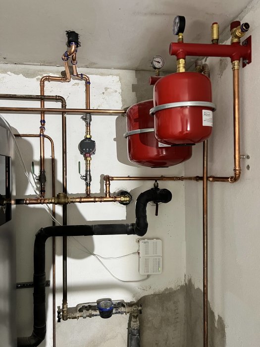 Välinstallerade rör och en säkerhetsventil i ett pannrum med kopparledningar och expansionskärl.