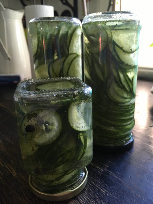 Två glasburkar med inlagda gurkskivor, svartpepparkorn, dill och habanerosalt.