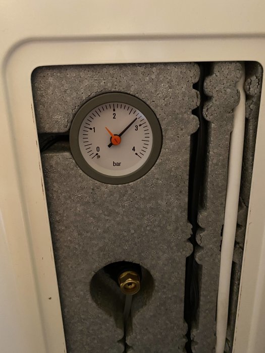 Tryckmätare med orange visare som visar cirka 1,5 bar, monterad bakom vit lucka på en Nibe F370 värmepanna.