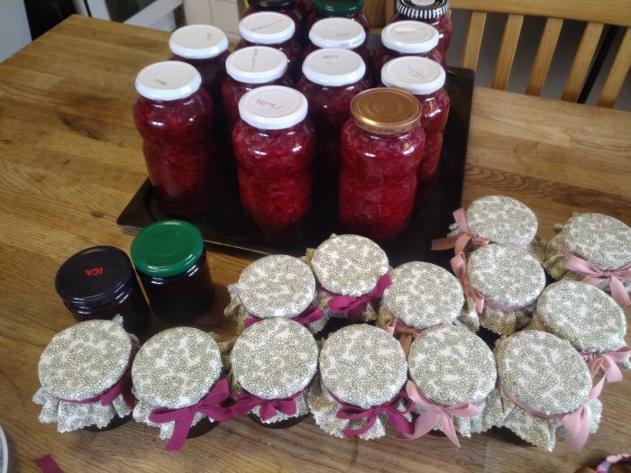 Hemmagjord sylt i glasburkar med tyglock och rosa band på ett träbord.