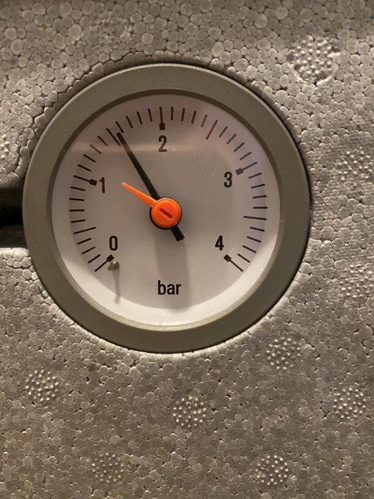 Tryckmätare för värmesystem visar ungefär 1,5 bar på en strukturerad bakgrund.