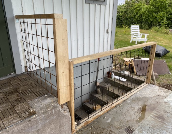 Nybyggt trästaket med svartmålat armeringsnät vid trappa för att förebygga fall.