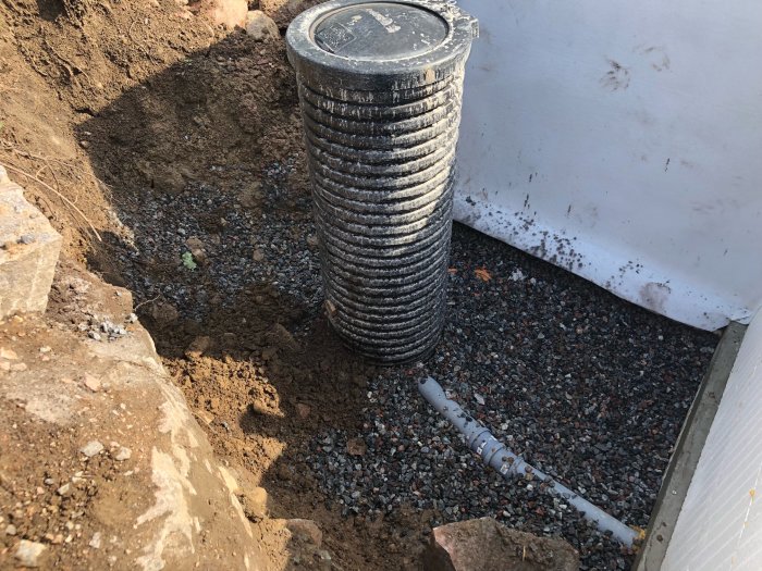 Nygrävd hålighet vid husvägg med avloppsrör och dräneringsbrunn för altantak och poolavvattning.