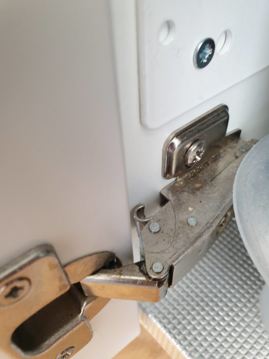 Närbild av ett trasigt köksskåpsgångjärn med bruten metallfjäder från Vedum kök.
