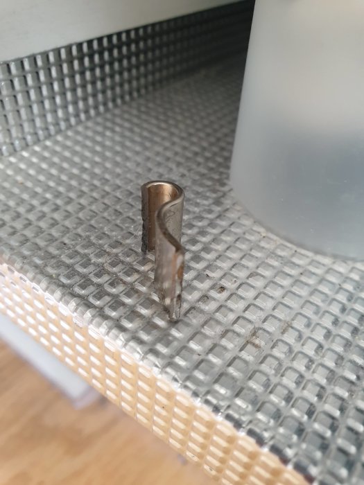 Brusten metallbit som liknar en fjäder på ett mönstrat golv, möjligen ett trasigt köksgångjärn.