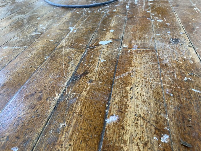 Slitet trägolv med tydliga repor och lackrester innan slipning och renovering.