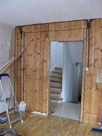 Seinässä on avattava oviaukko olohuoneeseen. Taustalla näkyy portaat. Vasemmalla on rakennusteline ja sahalaitteita.
