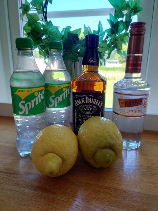 Flaskor med Sprite, Jack Daniels, De Kuyper Triple Sec och två citroner på ett bord.