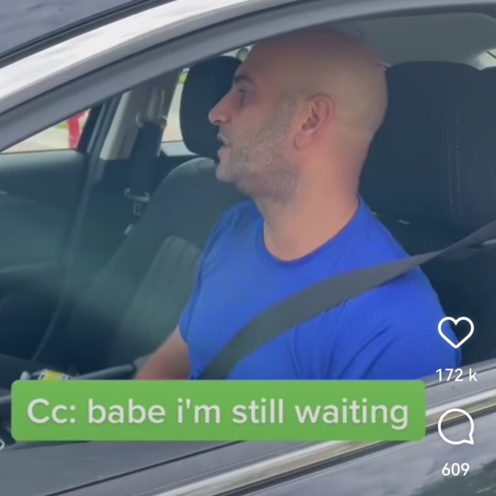 Man i blå tröja sitter förarsätet i bil, ser åt sidan, textremsa med "babe i'm still waiting".