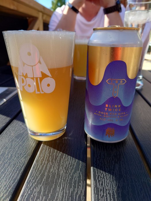 Ölglas och burk av Blink Twice Double IPA på träbord utomhus.