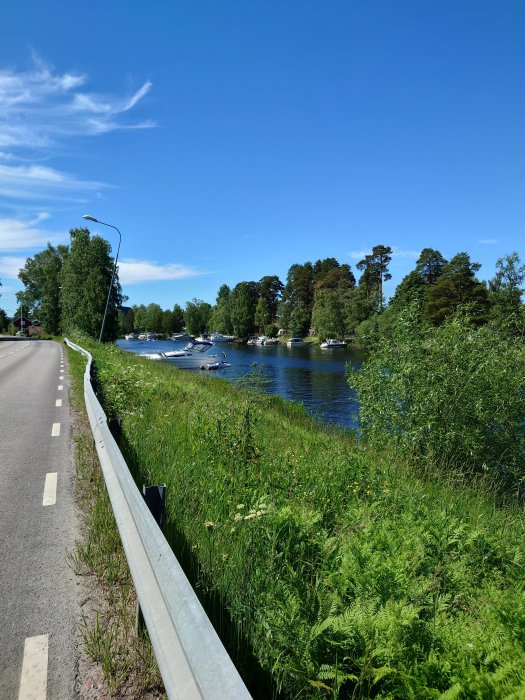 En lugn flod i Torsång med några båtar förtöjda längs kanten, omgiven av grönskande vegetation under en klarblå himmel.