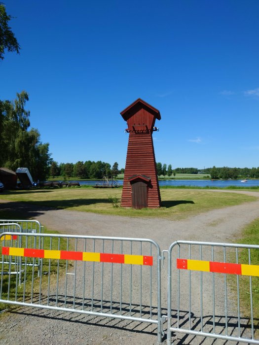 Rött trästapeltorn i Torsång vid en klarblå himmel, omgivet av grönt gräs och metallstaket före evenemang.