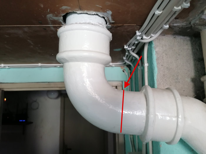 Vitmålat gjutjärns avloppsrör med röd linje där skärning övervägs för koppling till plaströr.