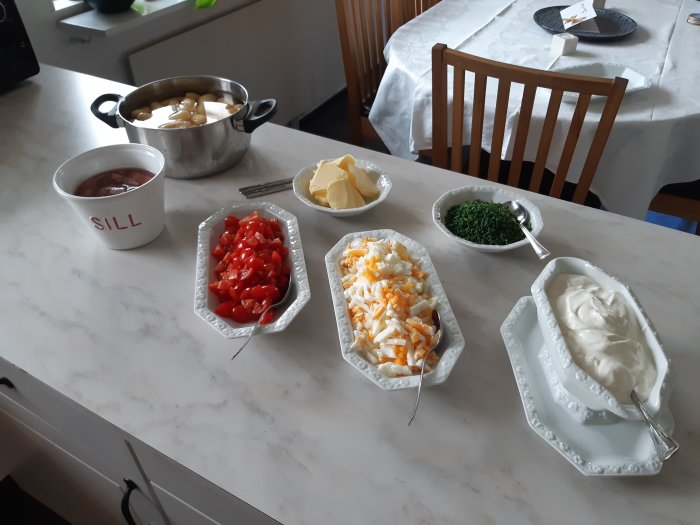 En dukat bord med svensk midsommarmat inklusive sill i en kruka, tärnade tomater, potatissallad, hackad gräslök och gräddfil.