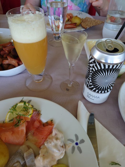 Ett festmåltid med lax, potatis och sås på en tallrik, ett glas öl och en burk Hallands Fläder på ett dukat bord.
