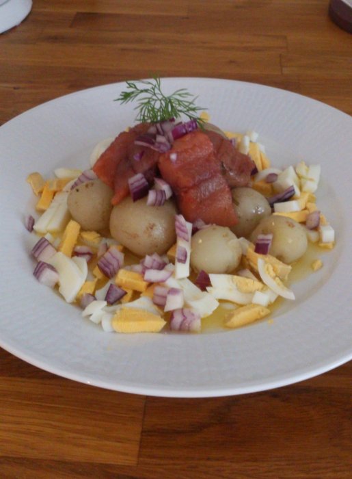 Midsommar-lunch med potatis, matjessill, rödlök, ägg och brynt smör på en vit tallrik.