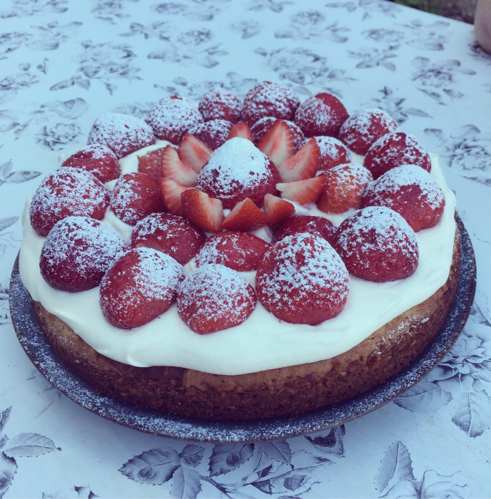 En sommartårta toppad med jordgubbar och florsocker på ett mönstrat bord.