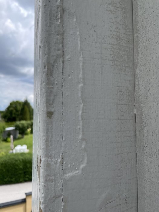 Närbild på ett trästaket med vit färg som flagnar, och synliga reparationer mot en suddig bakgrund.